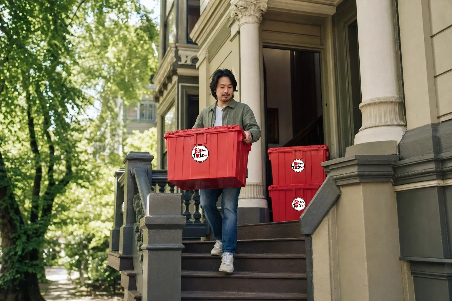 Person carrying a red moving tote down the steps of an ornate Alphabet District Victorian apartment building